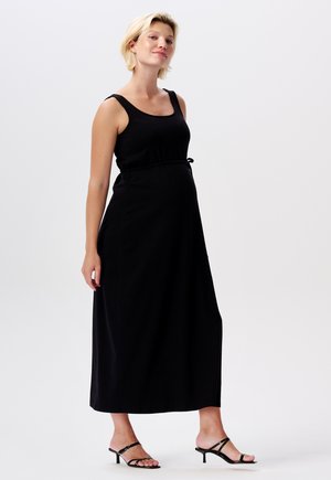 Zwarte mouwloze maxi-jurk met een verstelbaar koord in de taille, gemaakt van zachte stof. Draagt bij minimalistische zwarte hoge hakken sandalen.