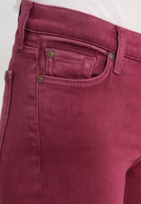 Maroon denim-housut, joissa on slim fit -leikkaus, viisi taskua, kuparinväriset yksityiskohdat sekä sileä rakenne, jossa on hieman joustoa.