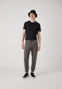 Camiseta negra de manga corta, pantalones grises con cordón, zapatillas negras y blancas, y un sombrero tipo bucket negro. Diseño minimalista con un ajuste cómodo.