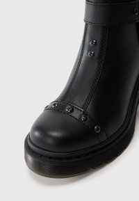 Stivaletto in pelle nera con punta arrotondata, borchie decorative argento lungo la cucitura e suola piatta con texture.