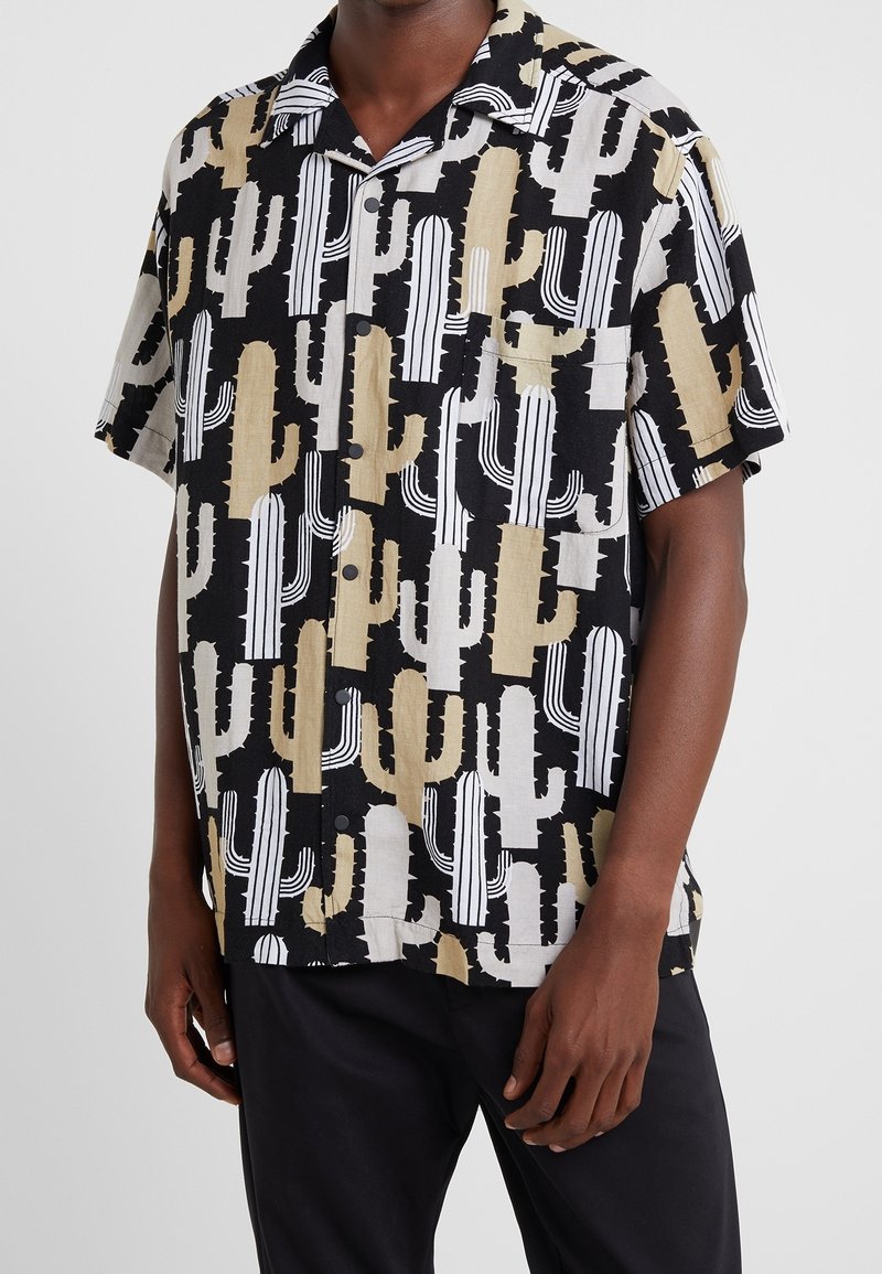 Chemise à manches courtes avec un motif de cactus en beige, noir et blanc. Fabriquée en tissu léger, avec un devant à boutons et un col.