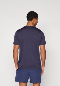 Marineblå kortermet treningstrøye med rund hals og jevn tekstur, kombinert med matchende shorts, sett fra baksiden.