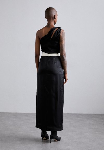 Melnas satīna kleitas ar vienu plecu, kas izceļas ar balto jostu. Garš, plūstošs siluets, gluda tekstūra un augstpapēžu melnas kurpes.