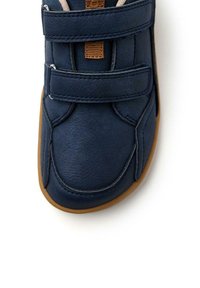 Chaussure en cuir bleu avec deux bandes auto-adhésives, une forme de bout arrondi et une semelle en caoutchouc brun flexible. Texture lisse avec des accents cousus.