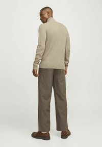 Beige geribde turtleneck trui met lange mouwen, gecombineerd met donkerbruine wijde broek. Bruine schoenen maken de outfit compleet.