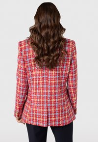 Rood en blauw geruite blazer met gouden accenten, met een gestructureerd ontwerp, op maat gemaakte pasvorm en een enkele knoopsluiting. Getextureerde stof zichtbaar.