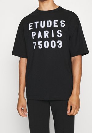 Czarna bawełniana koszulka z dużym białym napisem: "ETUDES PARIS 75003". Krótkie rękawy i luźny krój z okrągłym dekoltem.