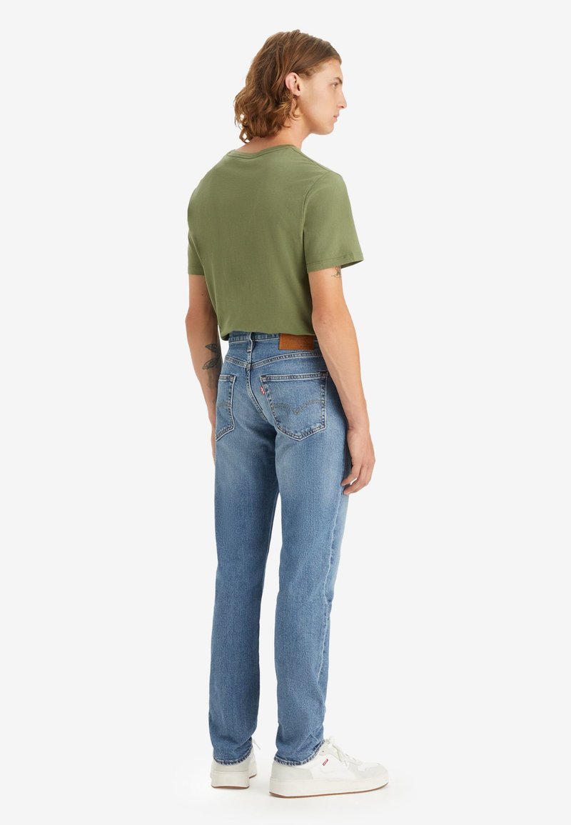 Camiseta verde oliva recortada combinada con jeans rectos de color azul claro. Zapatillas blancas con detalles mínimos y un parche de piel en color marrón claro.