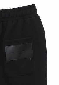 Pantalones de chándal negros con cintura elástica y un bolsillo de piel con texto grabado en la parte posterior. Tejido suave y texturizado.