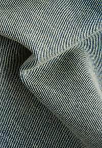 Tissu en denim présentant un motif sergé bleu et crème, affichant un poids moyen et une surface légèrement texturée.