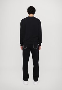 Felpa nera con maniche lunghe, polsini e orlo a coste; abbinata a pantaloni neri con cuciture a contrasto e vestibilità ampia.