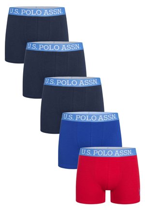 Man wearing a white sleeveless undershirt and blue U.S. Polo Assn. boxer briefs, standing barefoot against a plain white background.