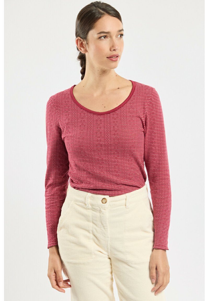 Haut rouge à manches longues avec de fines rayures blanches et un col rond, associé à un pantalon en velours côtelé de couleur claire avec des boutons sur le devant.