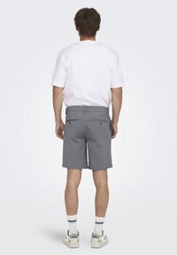 Pantaloni corti grigi con una texture liscia, dotati di due tasche posteriori e passante per la cintura, abbinati a una maglietta bianca e scarpe da ginnastica grigie.