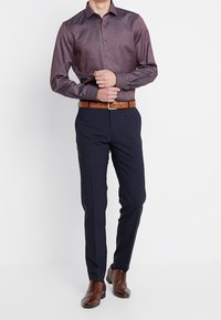 Camicia button-up bordeaux con un motivo testurizzato, abbinata a pantaloni navy. Cintura in pelle marrone e scarpe coordinate completano l'outfit.
