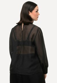 Zwarte sheer blouse met lange mouwen, een V-rug en een losse pasvorm, met een subtiele textuur en elastsiche manchetten.