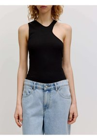 Zwarte, aansluitende tanktop met een asymmetrische halslijn, gemaakt van rekbaar materiaal, gecombineerd met lichtblauwe high-waisted jeans.