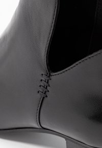 Stivale alla caviglia in pelle nera con finitura liscia, caratterizzato da cuciture decorative lungo il lato e un design con aperture.