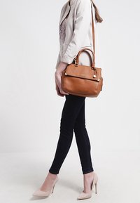 Brązowa skórzana torebka z podwójnymi uchwytami i odpinanym paskiem na ramię. Wyposażona w złote okucia i ma strukturę o wyraźnym kształcie.