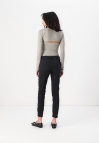 Åtsittande långärmad topp i ljusgrått med utskärning bak, kombinerad med svarta slim fit-jeans och svarta platta skor med silverfärgade öglor.