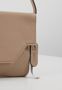 Sac bandoulière en cuir texturé beige avec rabat angulaire et lanière fine, présentant une petite étiquette en cuir embossée du mot "ESPRIT".