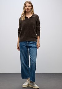 Maglione marrone, morbido e lavorato a maglia, con un collo a camicia, abbinato a jeans a gamba larga blu e sneakers dai toni chiari. Design minimalista.