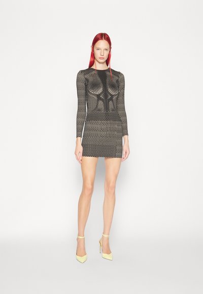 Zwarte mesh mini-jurk met lange mouwen en een strakke pasvorm, met een honingraatpatroon. Gecombineerd met gele hoge hakken.
