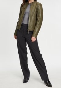 Olivgrön läderjacka med rund krage, framzipper och figursydd design; kombinerad med mörka vida byxor och svarta klackstövlar.