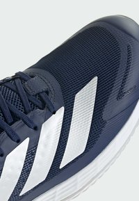 Chaussure de sport bleu marine avec des rayures blanches, fermeture à lacets et empeigne en maille texturée pour la respirabilité et le soutien.