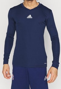 Tummansininen pitkähihainen urheilupaita, jossa on V-pääntie, valkoinen Adidas-logo rinnassa ja istuva malli, jossa on sileä pinta.