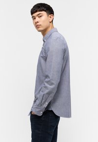 Koszula zapinana na guziki w jasnoniebieskim kolorze, wykonana z mieszanki bawełny. Posiada klasyczny kołnierzyk, długie rękawy oraz mankiety zapinane na guziki z zaokrąglonym dołem.
