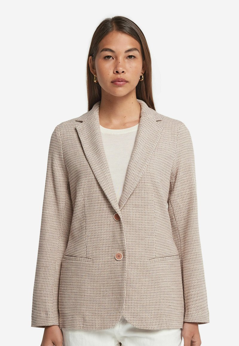 Beige texturerad kavaj med slag, två framfickor och två knappar. Materialet har ett subtilt vävt mönster.