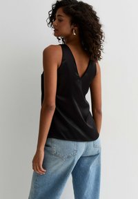 Zwarte satijnen mouwloze top met een V-hals ontwerp, gecombineerd met losse lichtblauwe denim jeans. Gladde textuur en ontspannen silhouet.