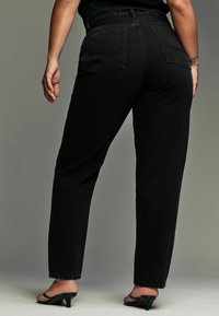 Zwart hoge taille denim jeans met een recht model, voorzien van achterzakken en subtiele stiksels. Gekleed met zwarte haksandalen.