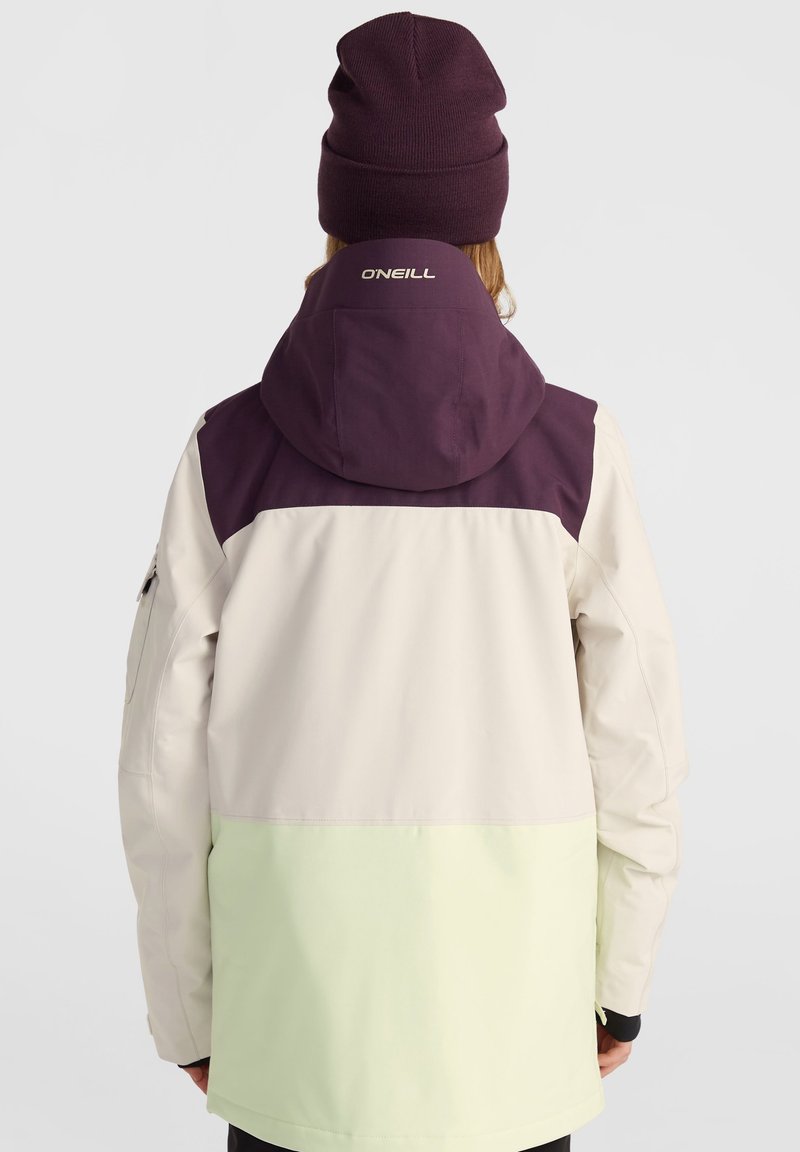 Kurtka w blokach kolorystycznych z ciemnofioletowym kapturem, jasnobeżową górną częścią i miętowo-zieloną dolną częścią. Posiada elastyczne mankiety oraz kieszeń na zamek.