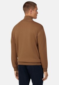 Brun stickad tröja med hög krage, ribbade ärmslut och nertill. Tyget verkar mjukt, med en figurnära design och subtila sömnadsdetaljer.