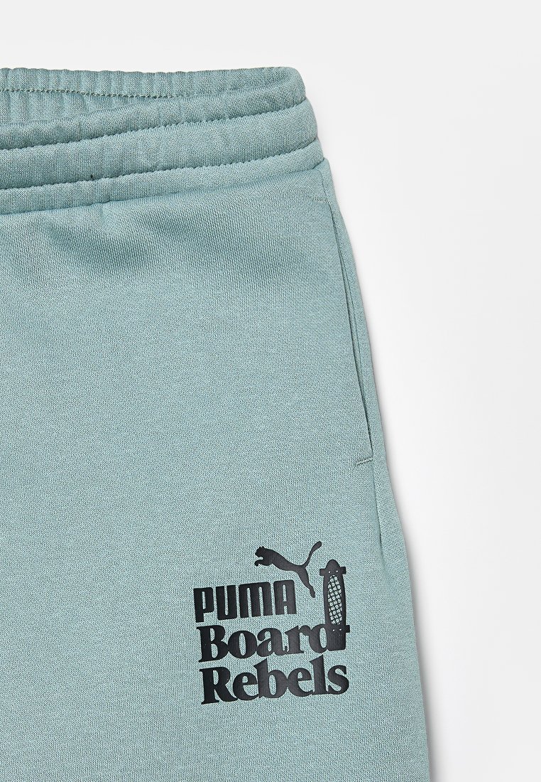 Pantaloni della tuta verde chiaro con vita elastica, dotati di un logo stampato nero che recita "PUMA Board Rebels" e il logo Puma.