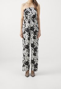 Mono sin mangas blanco y negro con estampado floral, con cintura elástica y diseño de pierna ancha, combinado con tacones beige de punta afilada.