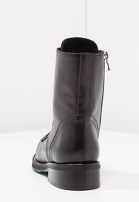 Černá kožená kotníková bota se zipem, s červeným prošíváním, kulatou špičkou a plochým podpatkem. Hladká textura a elegantní design.