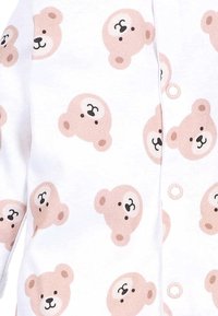 Baumwoll-Overall mit einem weißen Hintergrund, der mit wiederholten hellbraunen Bärenköpfen verziert ist. Bemerkenswerte Details sind kleine schwarze Augen und Knopfverschlüsse.
