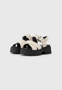 Chunky platform sandals with a black rubber sole, beige suede straps, silver buckle accents, and open toe design.