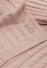 Suéter de punto rosa con canalé texturizado y patrones de trenza, adornado con pequeñas cuentas transparentes y un acento de logotipo circular dorado.