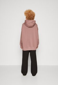Übergroßer rosa Hoodie mit hohem Kragen und großer Kapuze, kombiniert mit schwarzen weitem Bein Hose. Glattes, weiches Material, minimale Details.