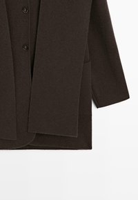 Manteau marron foncé en tissu doux, avec un col, deux boutons et des poches latérales. La coupe est droite avec un design épuré.