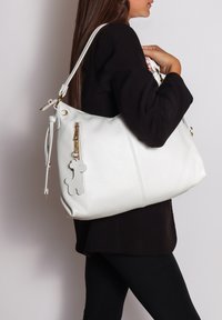 Witte leren handtas met een gestructureerde afwerking, voorzien van een gouden ritssluiting, een klein hondenvormig bedeltje en een lange, verstelbare schouderband.