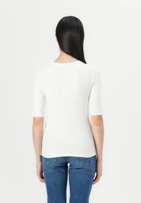 White ribbed knit top with short sleeves and a round neckline, paired with blue jeans. Features a fitted design and smooth texture.