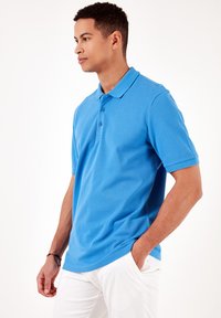 Camisa polo azul de algodón con cuello y tapeta de tres botones; mangas cortas; textura suave; aberturas laterales para un mejor ajuste.
