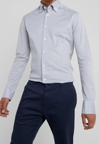 Jasnoniebieska koszula z długim rękawem i klasycznym kołnierzykiem, wykonana z teksturowanej tkaniny, w zestawieniu z ciemnogranatowymi spodniami.