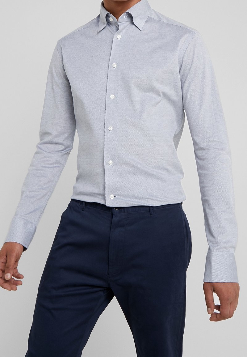 Jasnoniebieska koszula z długim rękawem i klasycznym kołnierzykiem, wykonana z teksturowanej tkaniny, w zestawieniu z ciemnogranatowymi spodniami.