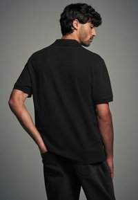 Polo nero con colletto, maniche corte e taglio dritto. Presenta una texture liscia senza motivi o dettagli visibili.